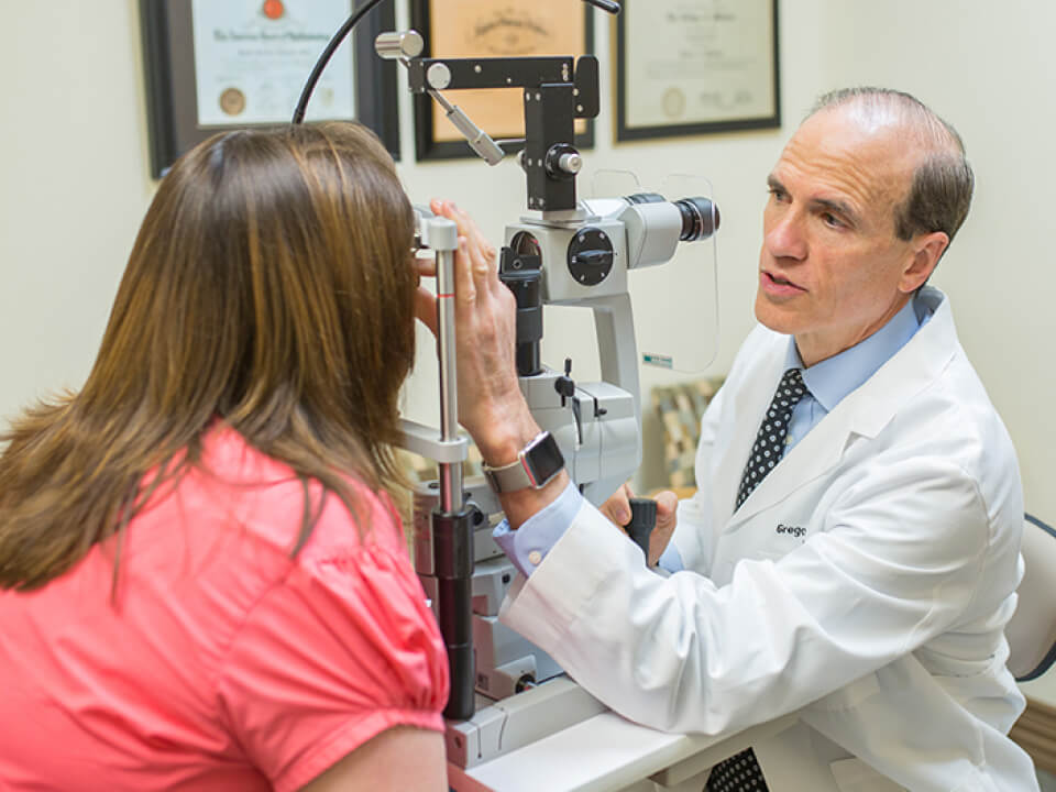 Eye doctor in a white coat performing an eye exam on a patient using a slit lamp in a medical office.
